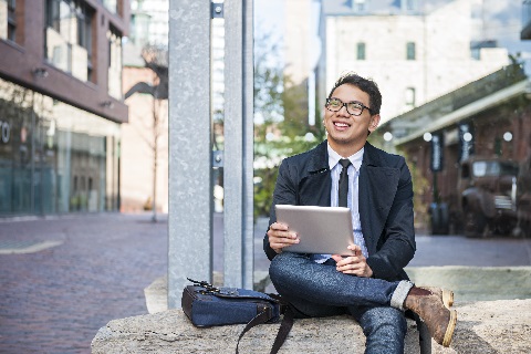 Young businessman sitting outside holding tablet